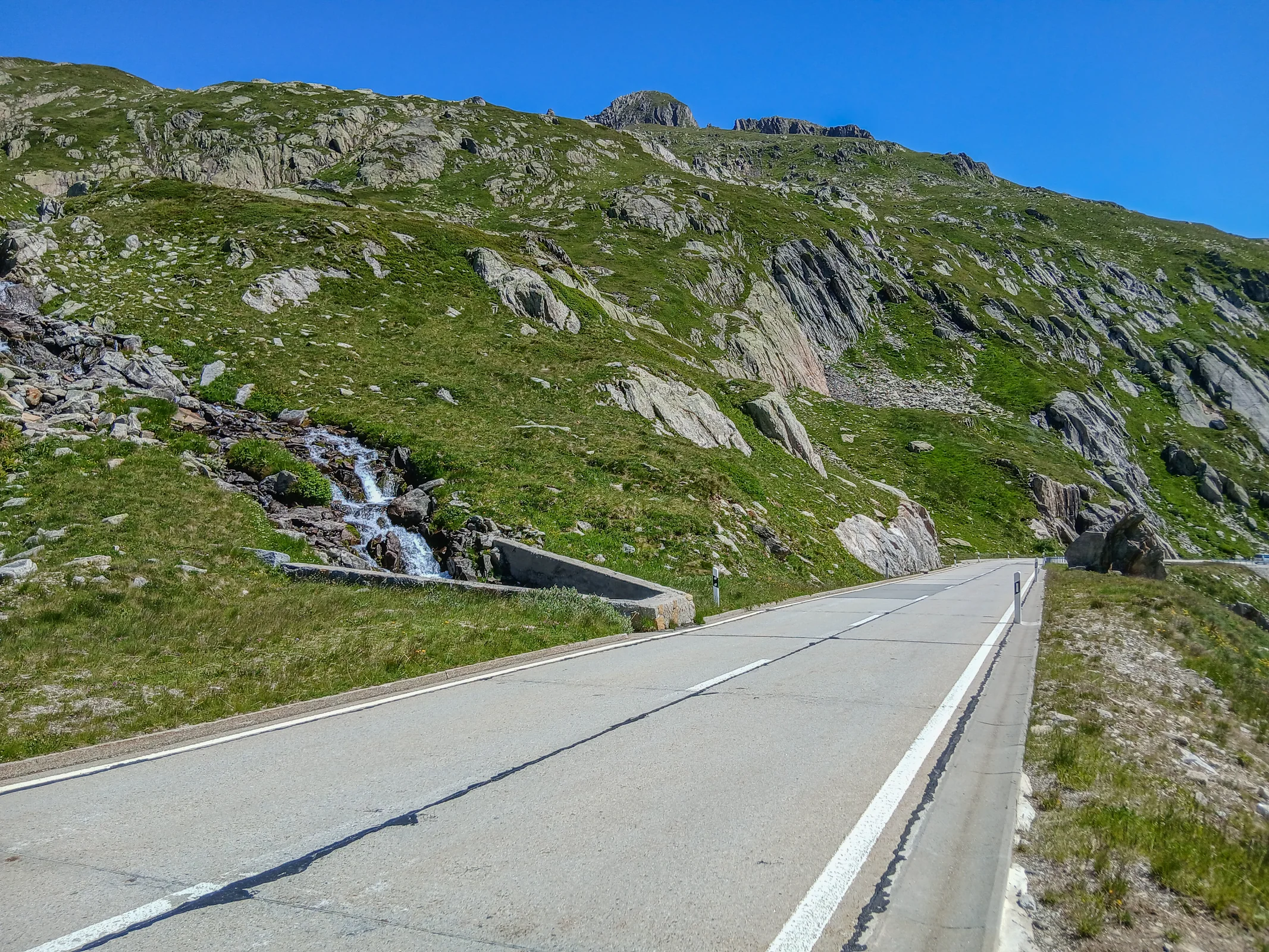 Die Nufenenpassstraße führt zwischen Granitfelsen und grünen alpinen Hängen zur Passhöhe